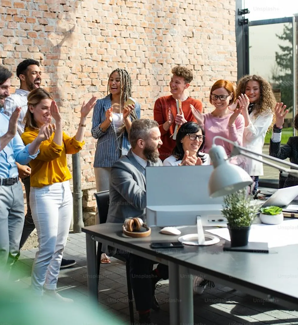 Een team applaudisseert enthousiast rond een collega aan een bureau buiten