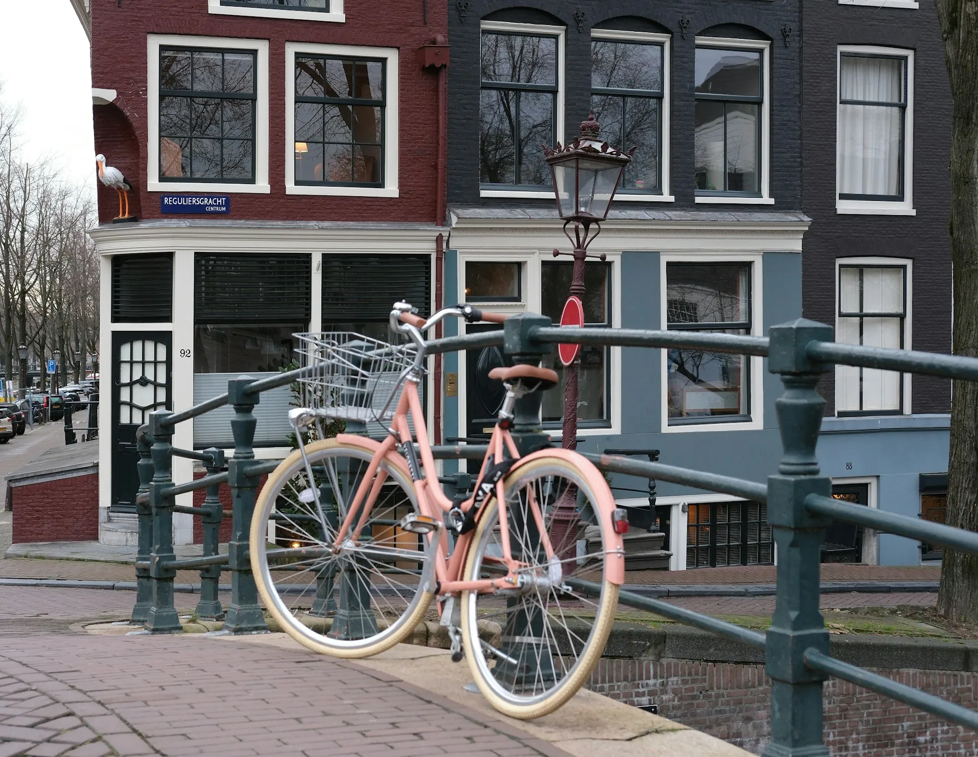 Een roze fiets tegen een brugleuning voor grachtenpanden