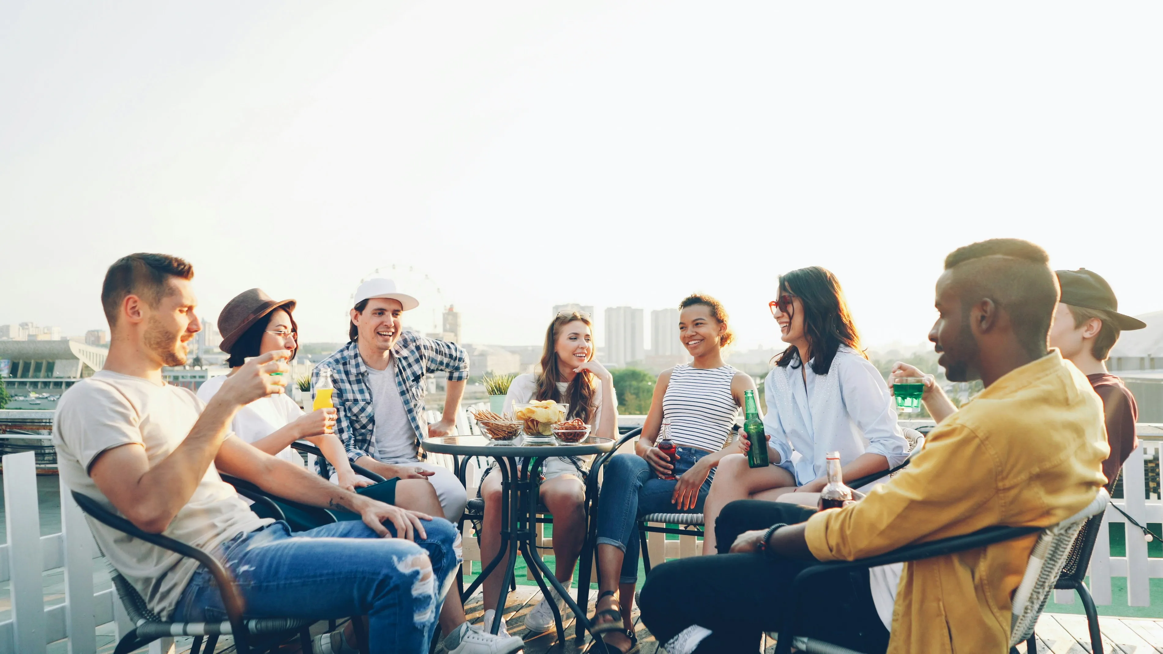 Een groep vrienden zit lachend samen aan tafel op een dakterras